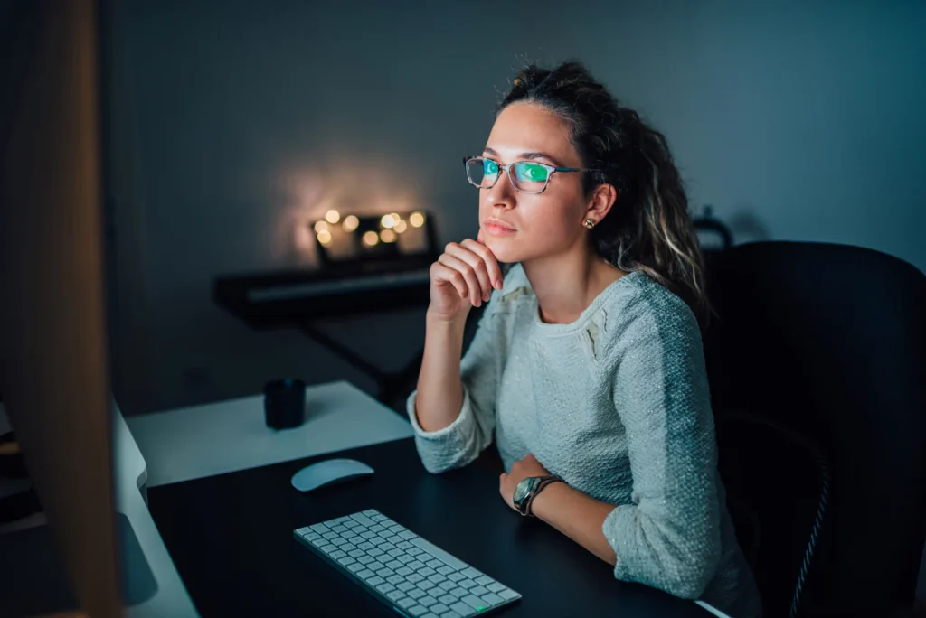 a woman sitting in front of her computer in a dimly lit room wearing glasses