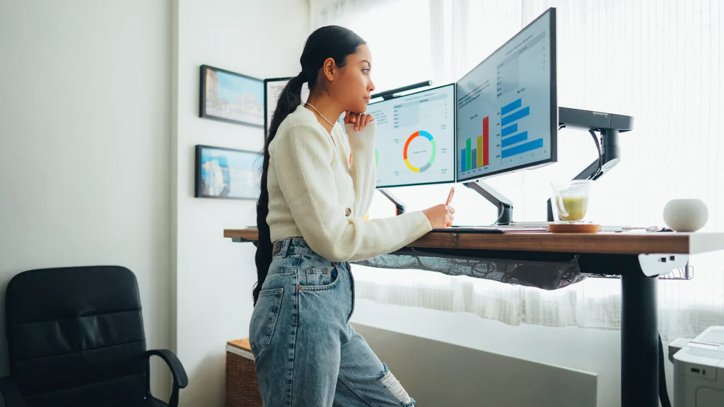 A woman standing in front of her standing desk in front of three computer monitors
