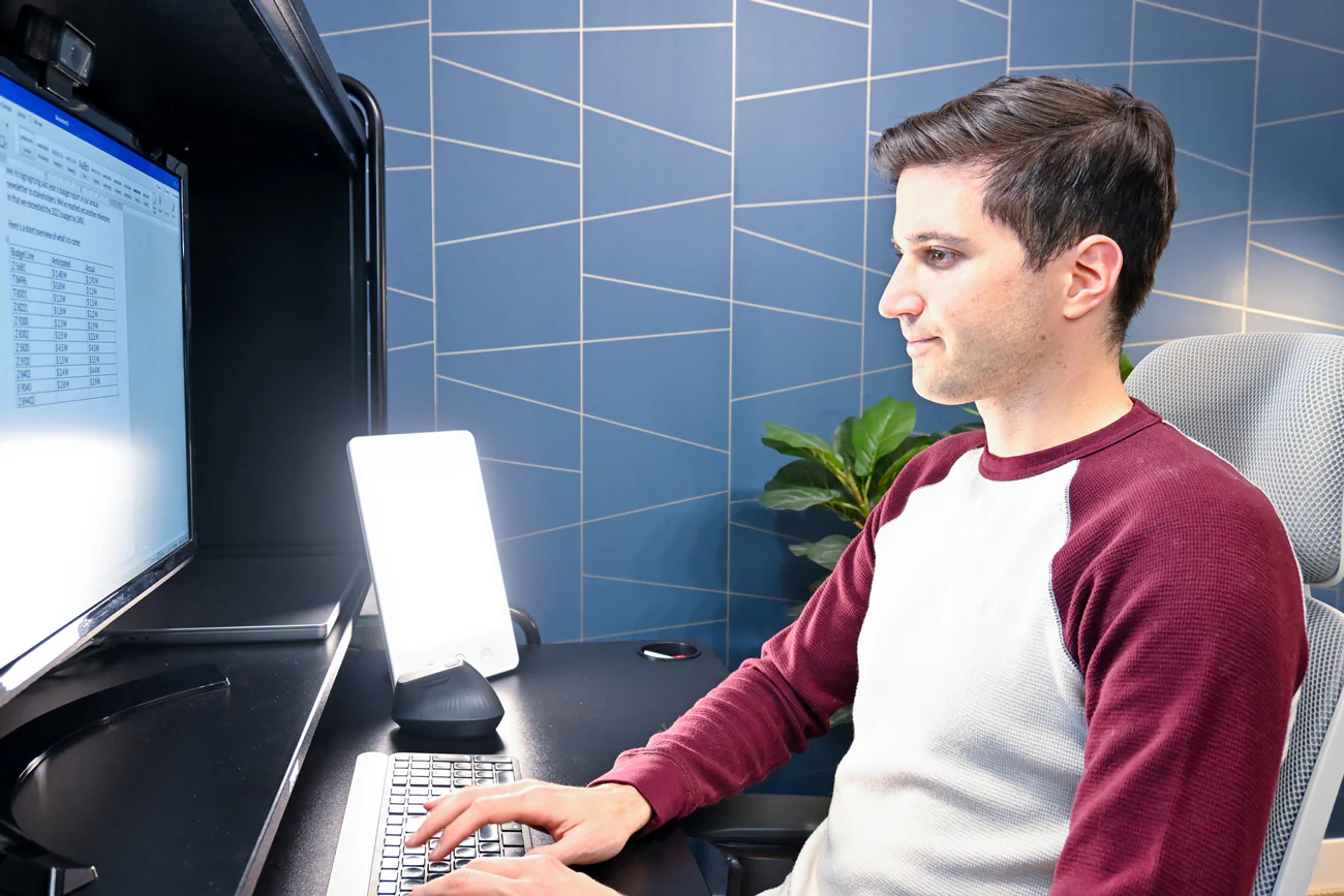 a young guy sitting in front of his computer using a happy lamp
